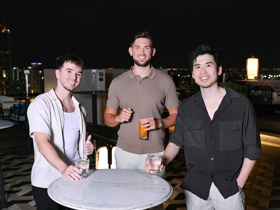 Three founders smiling at a rooftop table in Bangkok
