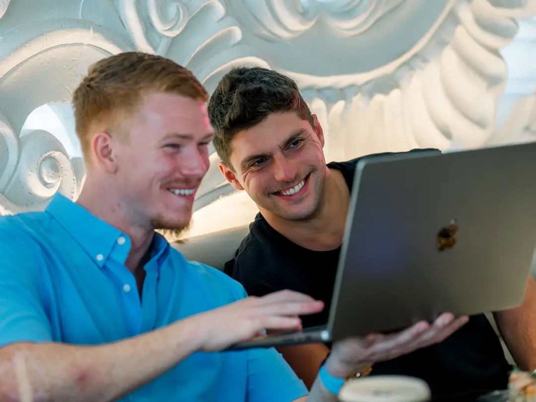 Two founders laughing over a laptop at a Reign dinner in Miami